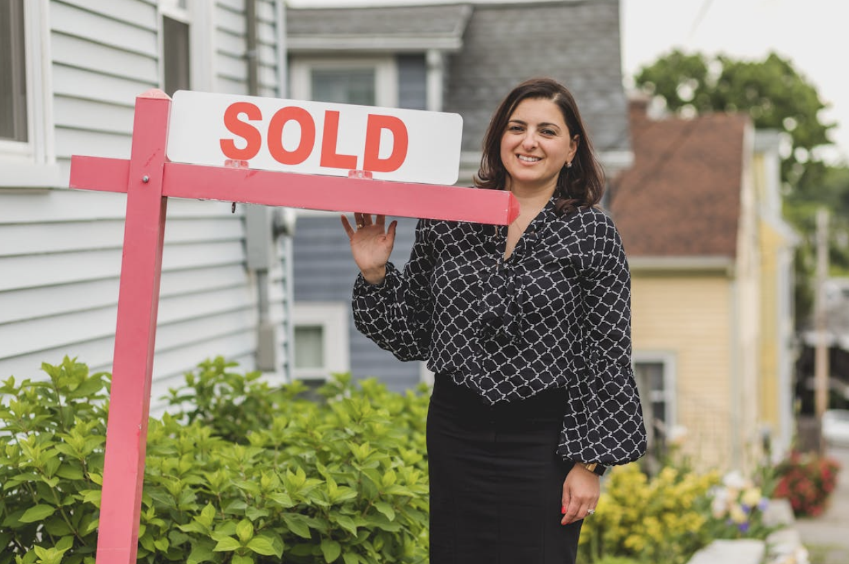 Smiling Female Real Estate Agent Standing Next to a Sold Sign